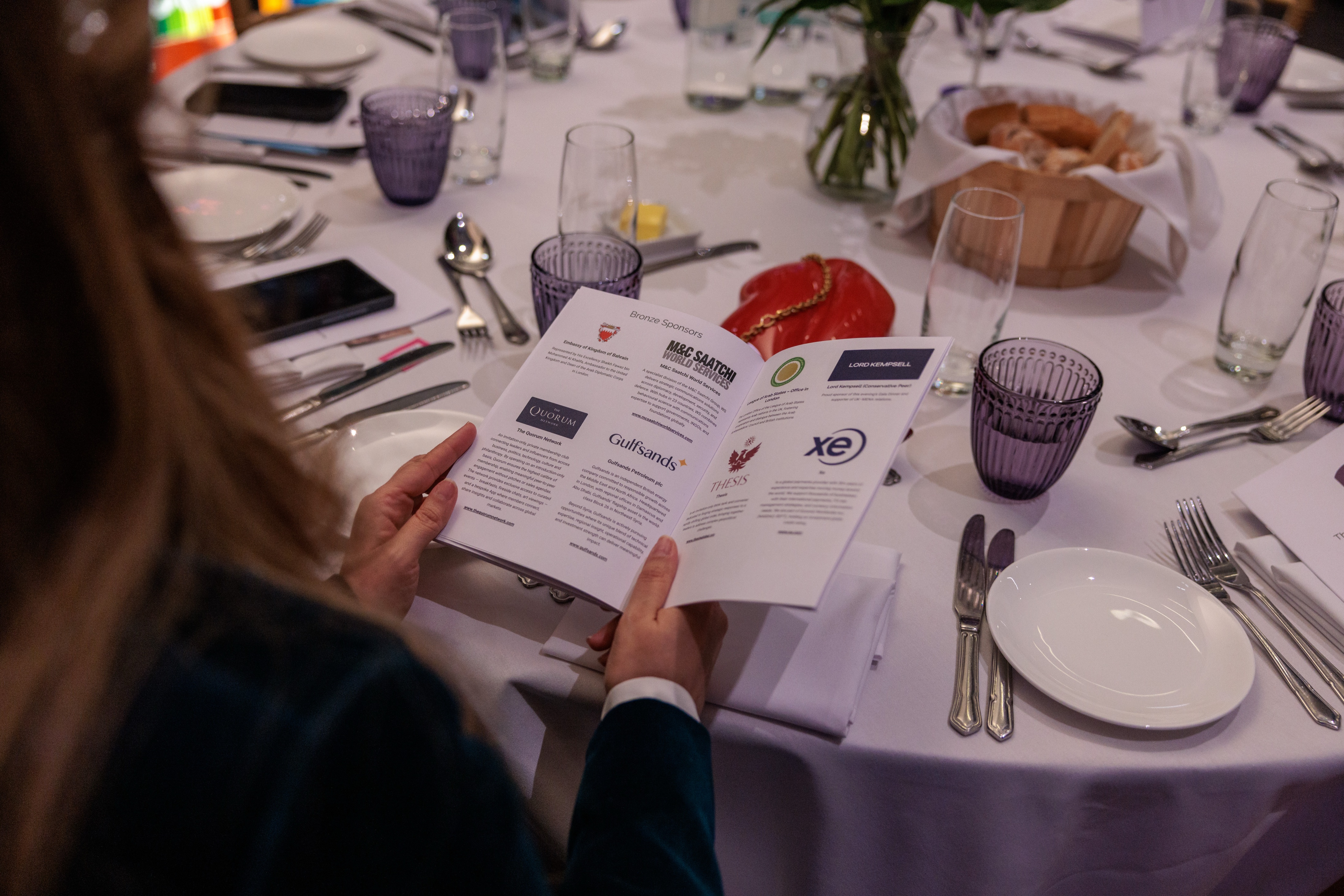 A guest reads the event brochure, open on the Bronze Sponsors page, at a beautifully set table